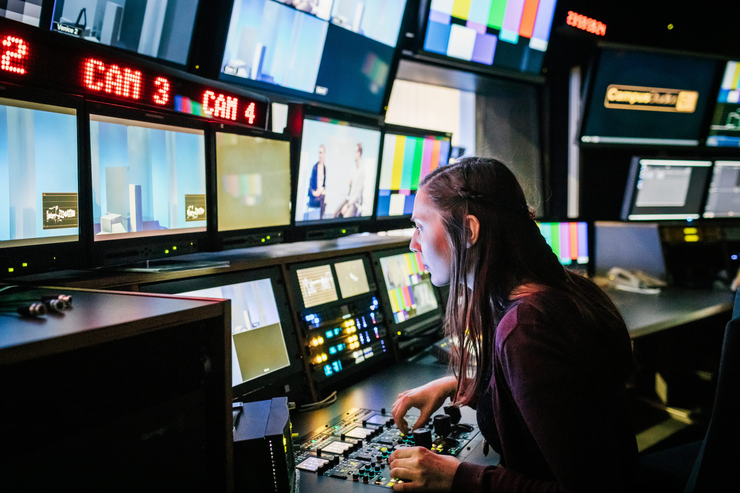 A university student looking at various screens while using tv studio equipment.
