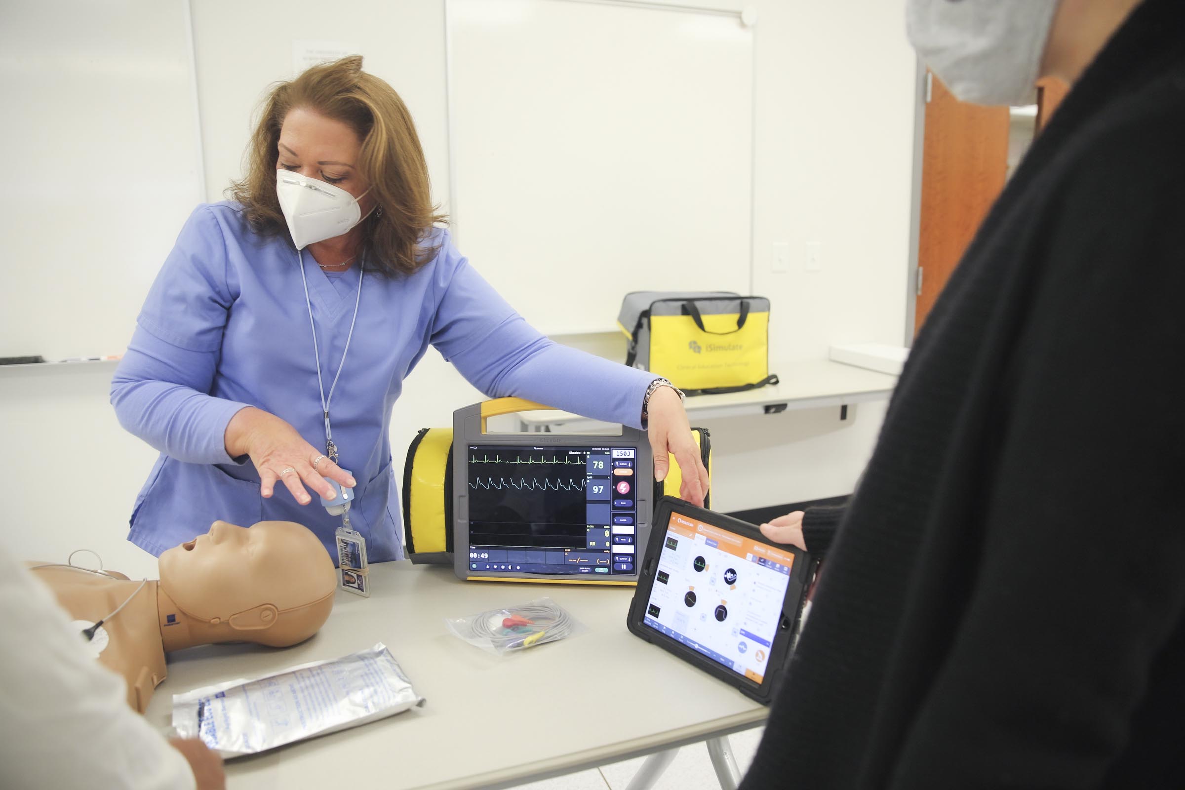 Karen Meadows stands over a patient simulation dummy demonstrating medical procedures.