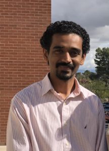 Man stands smiling in front of brick wall