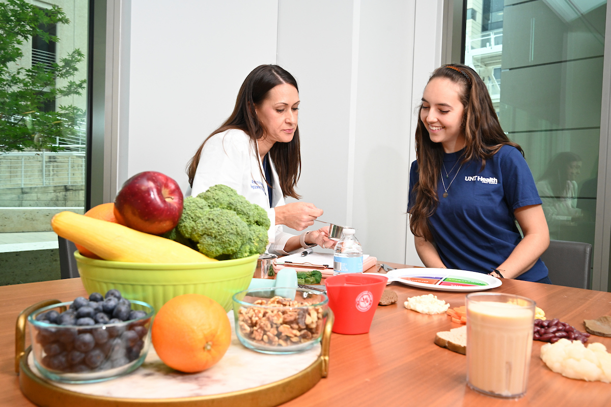 A UNT Health faculty member discusses nutrition with a student, with fresh fruits, vegetables and healthy foods displayed on the table.