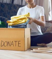 Woman Holding Clothes With Donate Box In Her Room, Donation Conc
