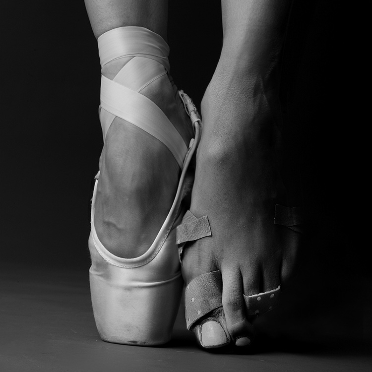 two feet pointed in a ballerina pirouette, the left is in a slipper the right has several bandaids