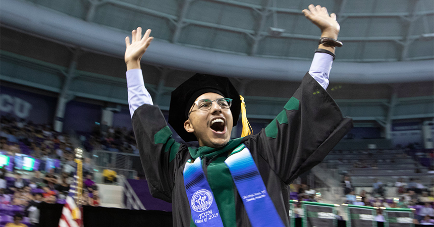 TCOM student raises both hands in the air in celebration during Commencement