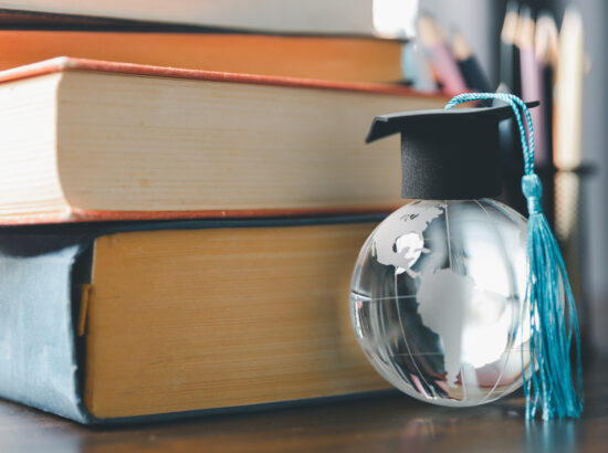 Graduate Study Abroad Program Concept : Black Graduation Cap On A Globe Map And Books, Depicts Knowledge Can Be Learned Online Anywhere And Everywhere, Even In Universities Or Campus Around The World.