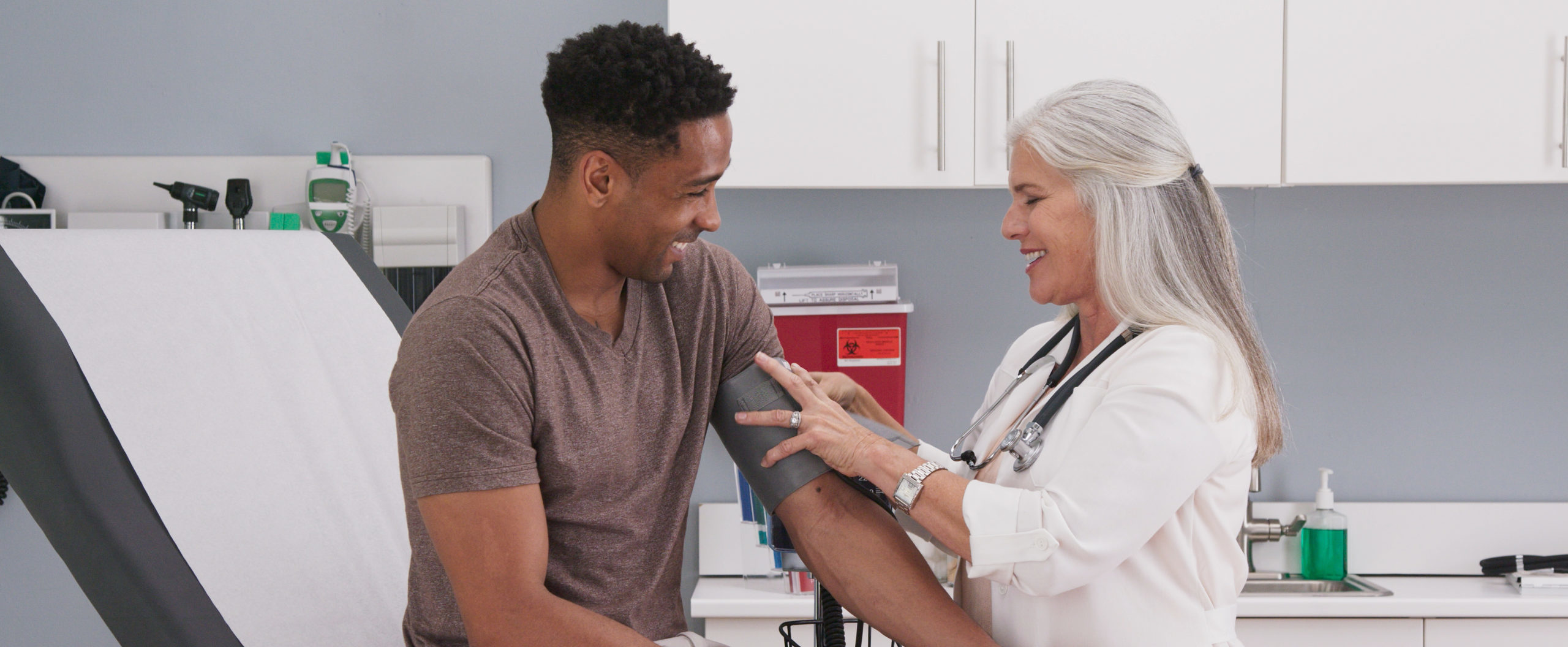 Mature White Female Physician Checking Male Patients Blood Pressure At Clinic