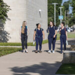 Photograph of four students in blue scrubs walking on a sidewalk.