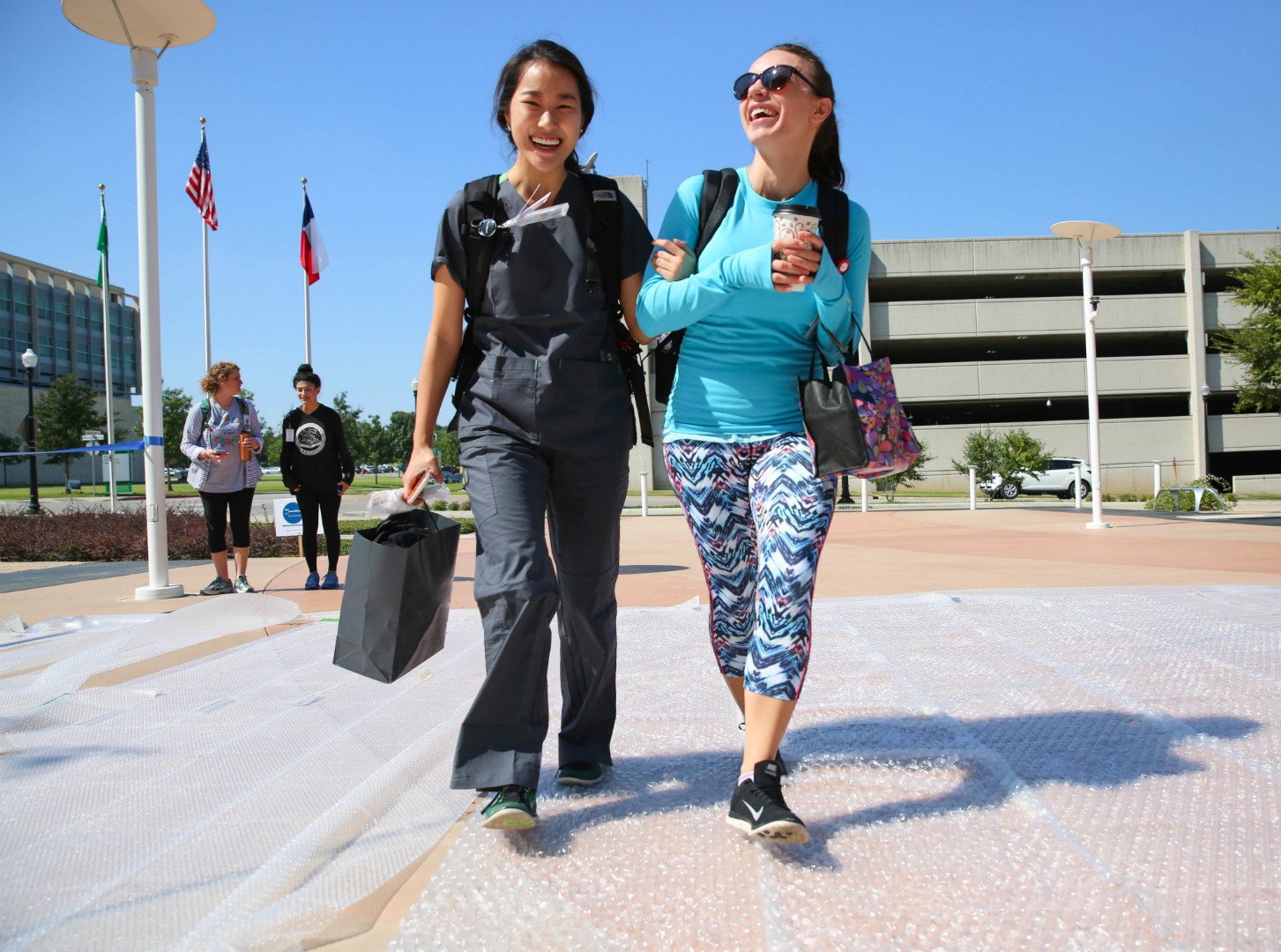 two unthsc students walking arm in arm across the bubble wrap laid out for "relieve your stress" day.