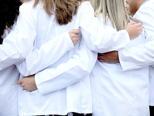 tcom students in white coats with arms around each other